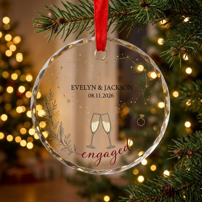 Round faceted glass ornament with gold constellation heart, ring, and clinking champagne flutes reading engaged.