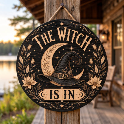 Round wooden sign with 'THE WITCH IS IN' slogan, crescent moon, witch hat, floral borders, stars and scrollwork.