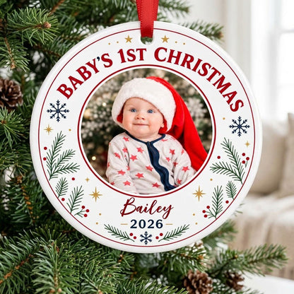 Round ceramic ornament with 'BABY'S 1ST CHRISTMAS', pine sprigs, snowflakes, gold stars, red rings, and a photo frame
