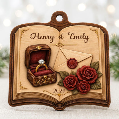 Open book wood ornament with a ring box, red roses, wax-sealed envelope, and custom names and year.