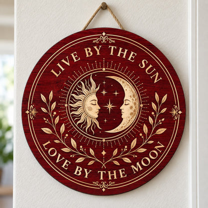 Round wooden sign with sun and crescent moon faces, stars, vines, and the quote Live by the Sun, Love by the Moon.