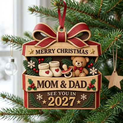 Gift box-shaped wood ornament with red bow, baby booties, teddy bear, and 'Mom & Dad See You In 2027' text.