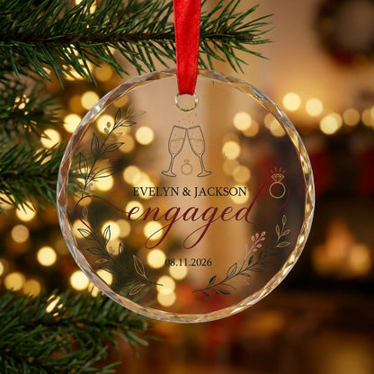 Round glass ornament with clinking champagne flutes, sparkles, ring and botanical foliage with burgundy ribbon and the w