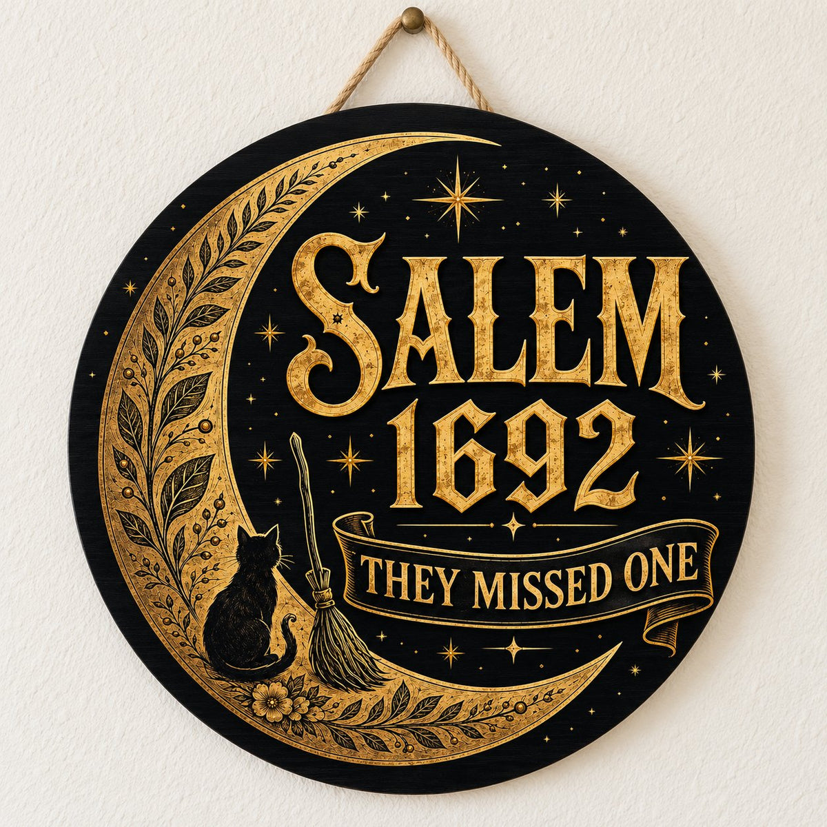Round wooden sign with gold crescent moon, black cat, broomstick, stars and 'SALEM 1692 THEY MISSED ONE' on black.