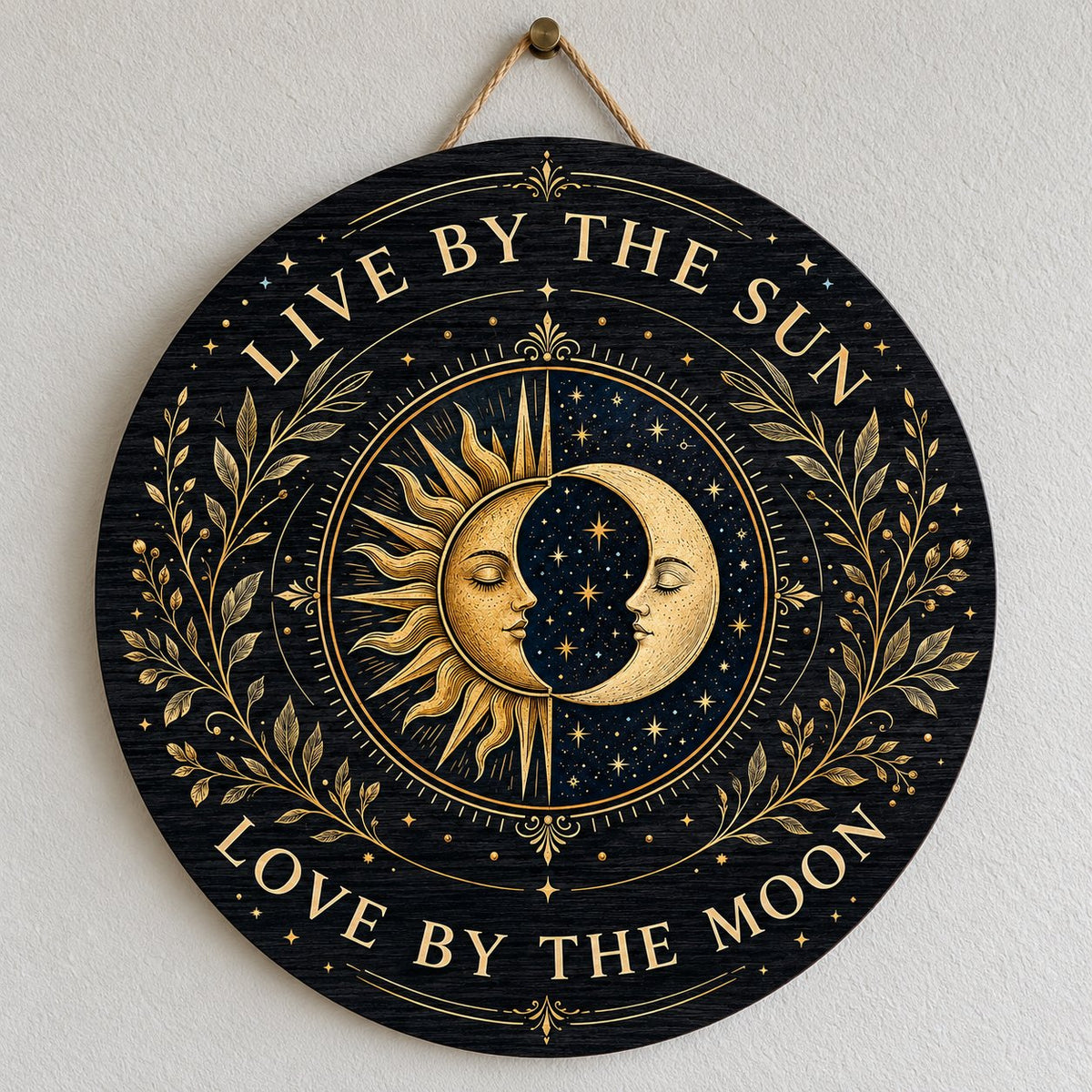 Round wooden sign with gold sun and crescent moon faces and the words “Live By The Sun, Love By The Moon”.