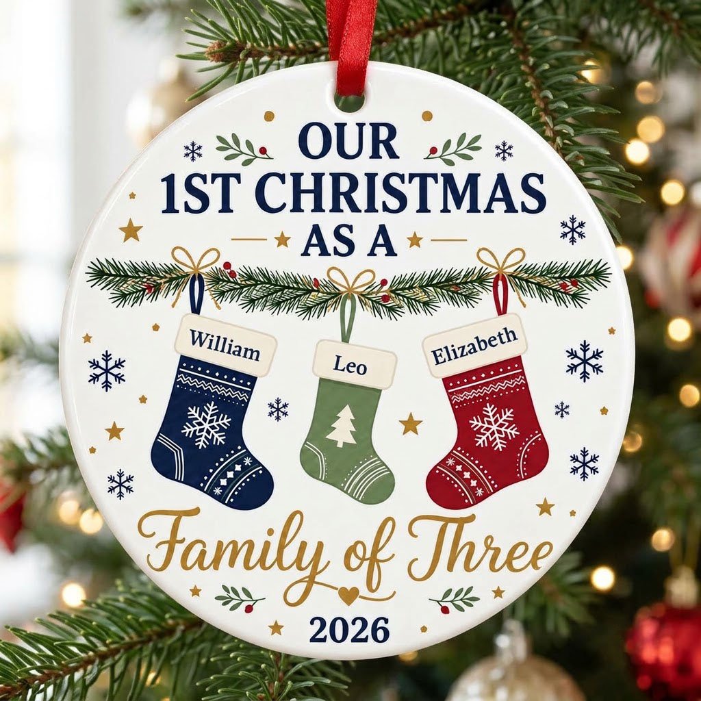 Round white ceramic ornament with garland, three stockings, and 'OUR 1ST CHRISTMAS AS A Family of Three 2026' text with 