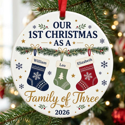 Round white ceramic ornament with garland, three stockings, and 'OUR 1ST CHRISTMAS AS A Family of Three 2026' text with 