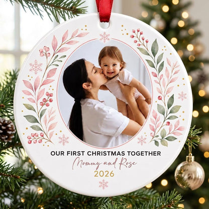 Round ceramic ornament with a photo frame, pink-green botanical wreath, and 'OUR FIRST CHRISTMAS TOGETHER' text.