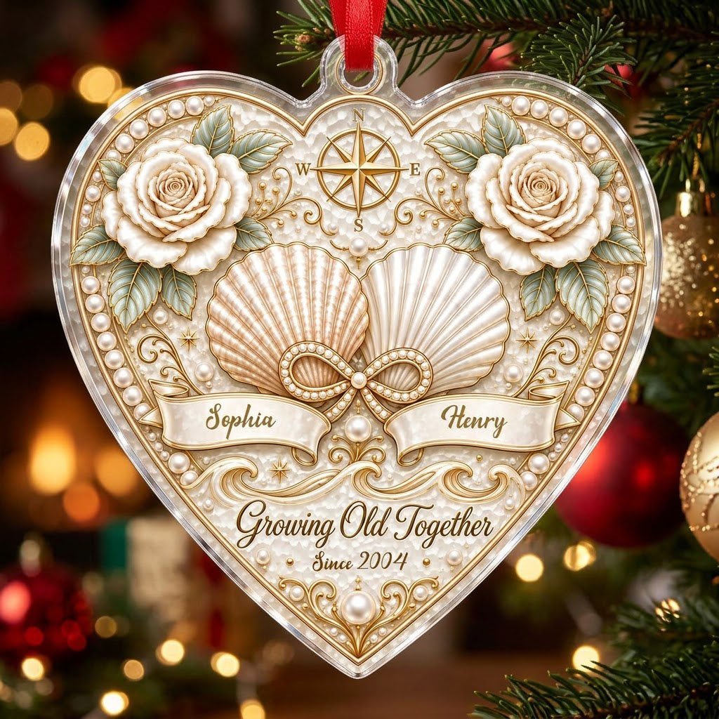 Heart-shaped clear acrylic ornament with seashells, pearl infinity symbol, compass star, and two name ribbons.
