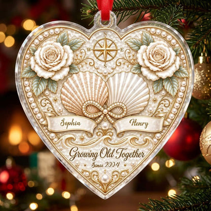 Heart-shaped clear acrylic ornament with seashells, pearl infinity symbol, compass star, and two name ribbons.