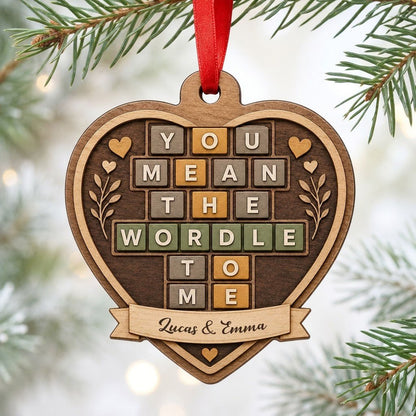 Heart-shaped wood ornament with Wordle-style tiles reading You Mean The Wordle To Me and names on a bottom banner.
