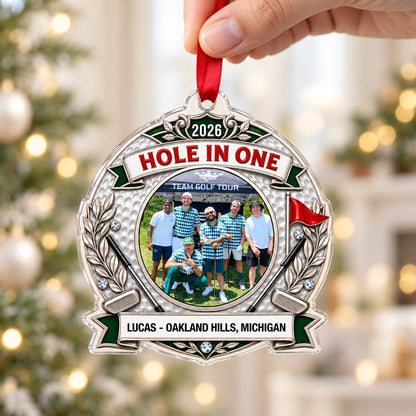 Silver trophy-style golf ornament with laurel branches, crossed clubs, red flag, 2026 and HOLE IN ONE, plus a circular p