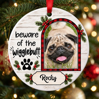 Round ceramic ornament with buffalo plaid photo frame, paw-heart, pine sprigs, and 'beware of the Wigglebutt'.