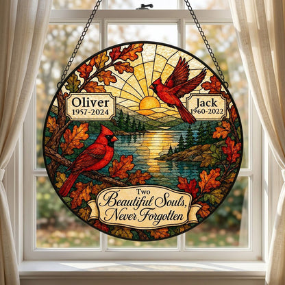 Two red cardinals with a glowing sun over a mountain lake and pine trees, framed by autumn oak leaves on a round suncatc