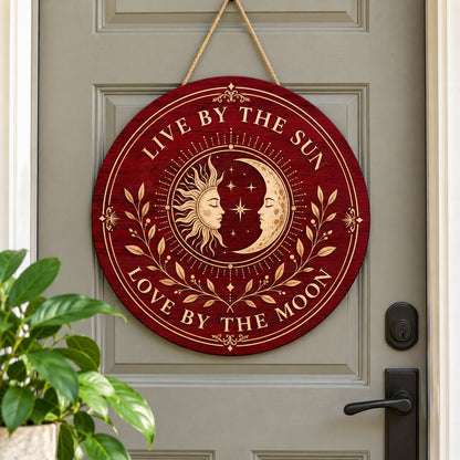Round wooden sign with sun and crescent moon faces, stars, vines, and the quote Live by the Sun, Love by the Moon.