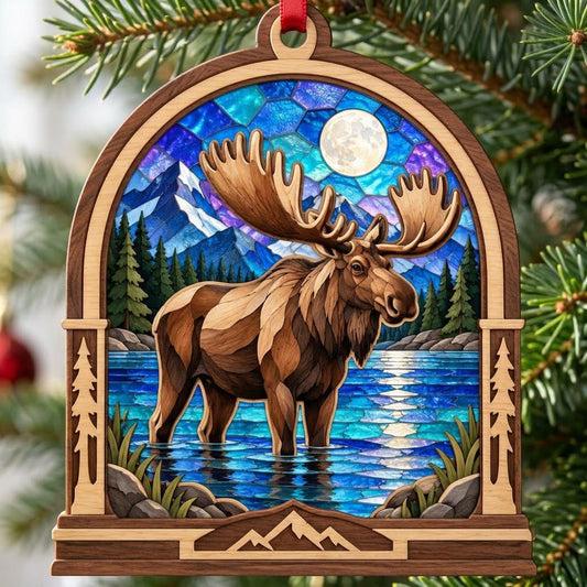 Arched wood ornament with a moose in water, pine trees, mountains, and a blue-purple stained-glass sky with a full moon.