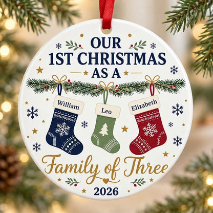 Round white ceramic ornament with garland, three stockings, and 'OUR 1ST CHRISTMAS AS A Family of Three 2026' text with 
