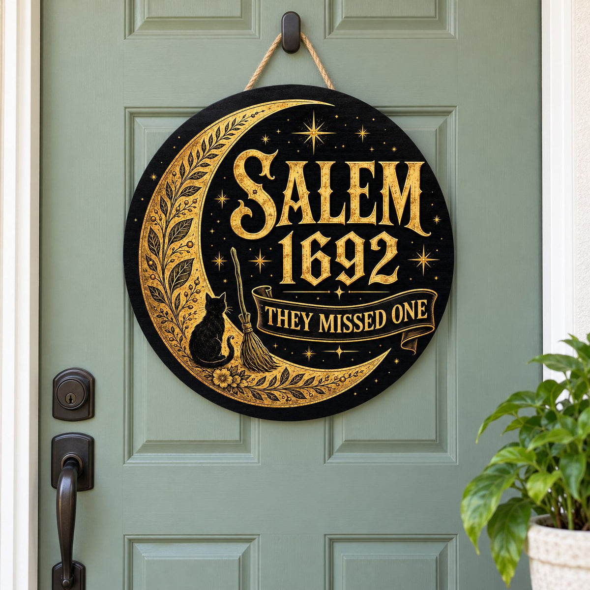 Round wooden sign with gold crescent moon, black cat, broomstick, stars and 'SALEM 1692 THEY MISSED ONE' on black.