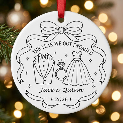 Round white ceramic ornament with black line art of bow, tuxedo, ring, dress, and THE YEAR WE GOT ENGAGED banner.