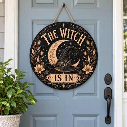 Round wooden sign with 'THE WITCH IS IN' slogan, crescent moon, witch hat, floral borders, stars and scrollwork.