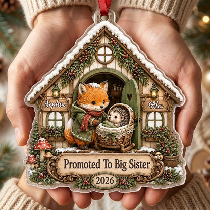House-shaped acrylic ornament with 'Promoted To Big Sister' and a fox beside a baby hedgehog in a bassinet.