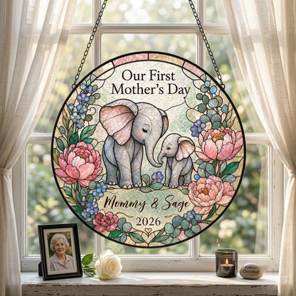Round stained-glass suncatcher of mother and baby elephants touching trunks amid pink peonies and blue flowers.