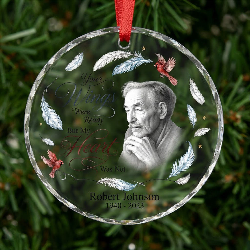 Round glass ornament with sketch portrait, two red cardinals, blue and brown feathers, and memorial name and years.