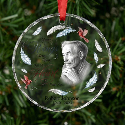 Round glass ornament with sketch portrait, two red cardinals, blue and brown feathers, and memorial name and years.