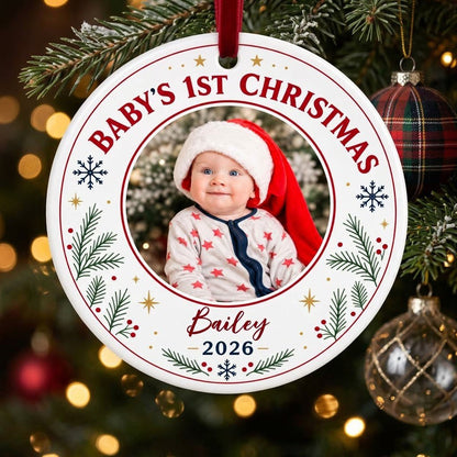 Round ceramic ornament with 'BABY'S 1ST CHRISTMAS', pine sprigs, snowflakes, gold stars, red rings, and a photo frame