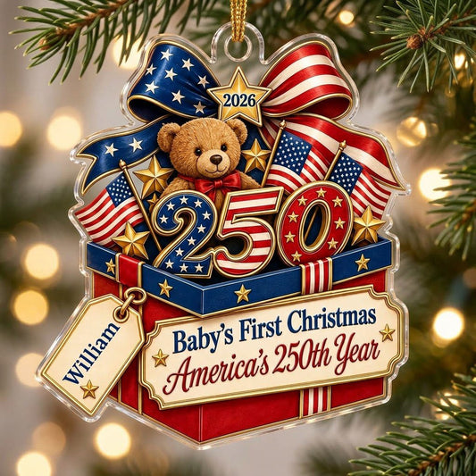 A teddy bear in a red gift box with blue trim, 250 and 2026 with American flags and a patriotic bow on an acrylic orname