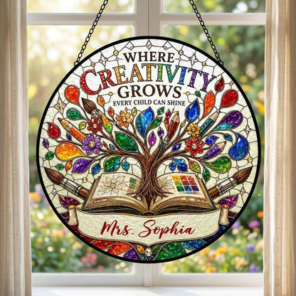 Round stained glass-style suncatcher with tree growing from an open book, paintbrushes, pencils, blossoms, and teacher n