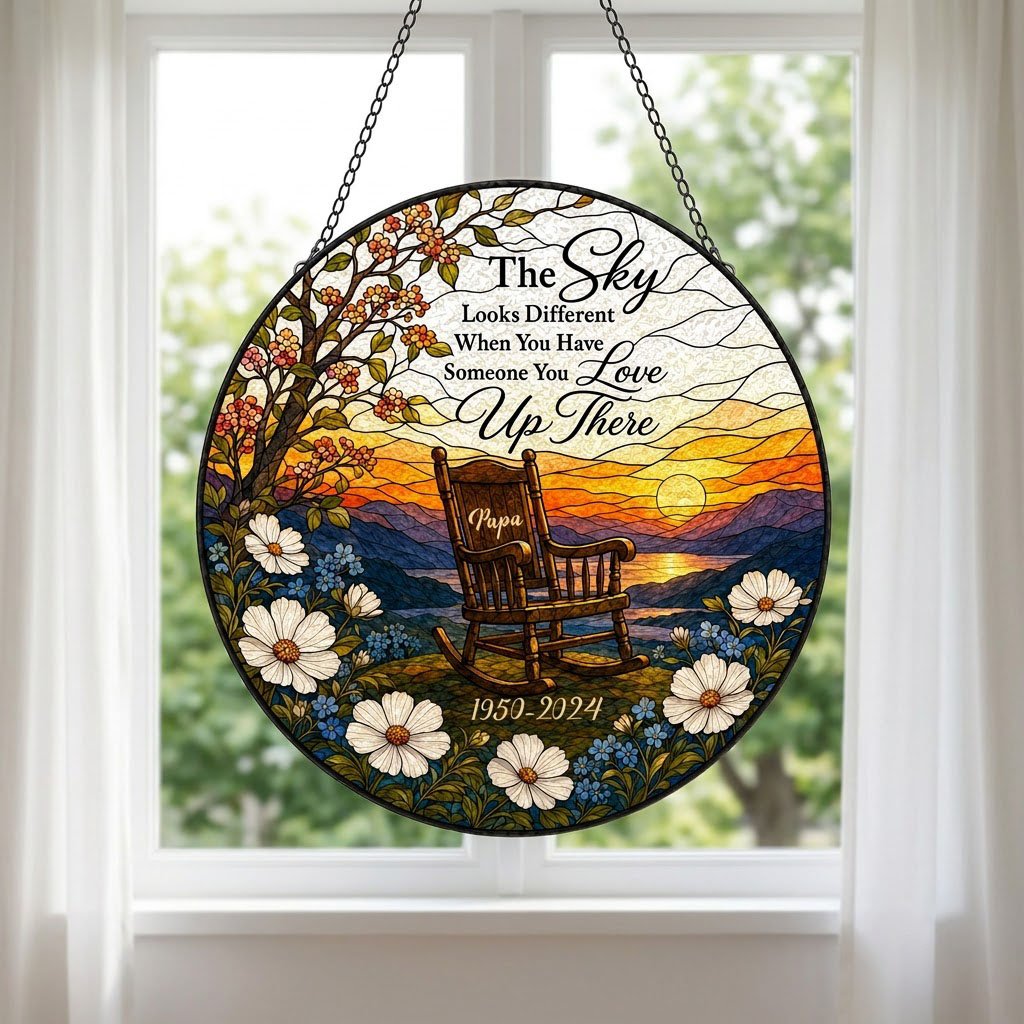 Round stained glass–style suncatcher with an empty rocking chair on a hill at sunset with flowers and a lake.