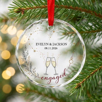 Round faceted glass ornament with gold constellation heart, ring, and clinking champagne flutes reading engaged.