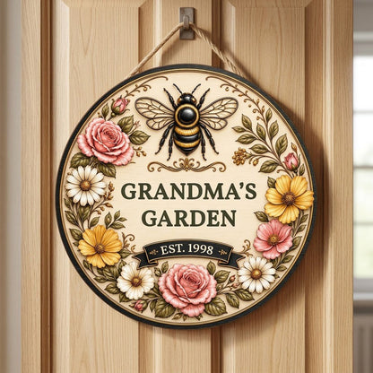 Round wooden sign with 'GRANDMA'S GARDEN', a gold-and-black bee, floral wreath, and EST. year on a light wood background