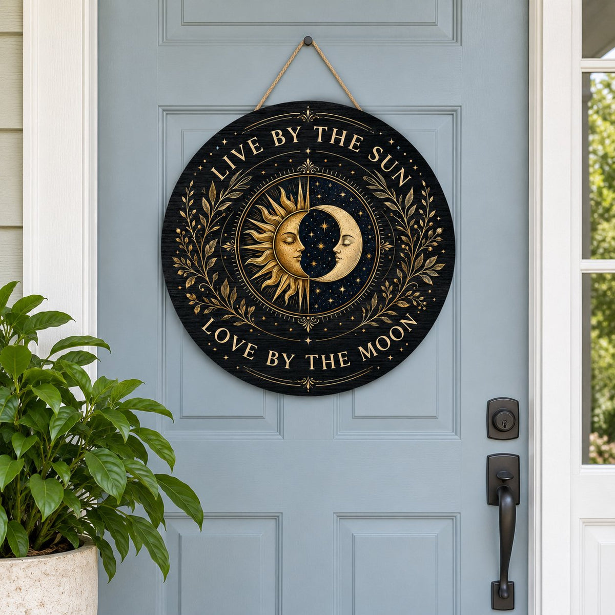 Round wooden sign with gold sun and crescent moon faces and the words “Live By The Sun, Love By The Moon”.