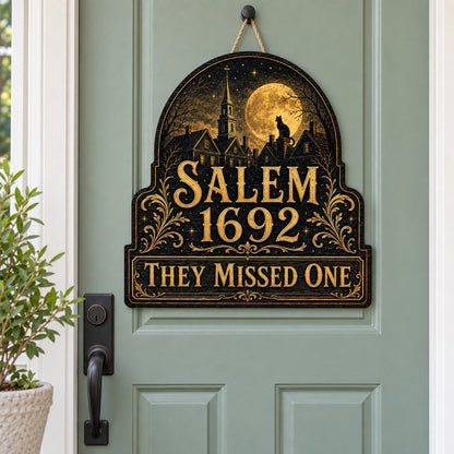 Custom-cut wooden sign reading “SALEM 1692” and “THEY MISSED ONE” with a black cat on a moonlit village and gold filigre