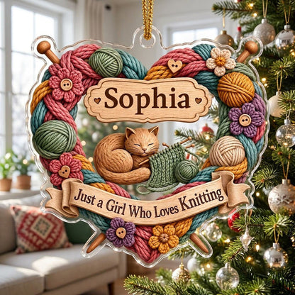 Heart-shaped acrylic ornament with yarn wreath, knitting needles, brown cat and "Just a Girl Who Loves Knitting" text.