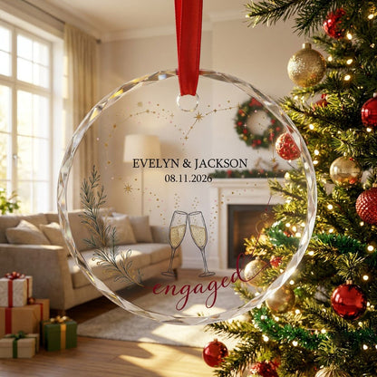 Round faceted glass ornament with gold constellation heart, ring, and clinking champagne flutes reading engaged.