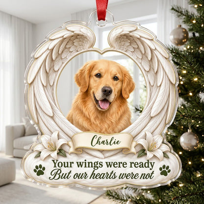 Clear acrylic angel wings ornament with a circular dog photo, white lilies, a dark green paw print, and a name banner.
