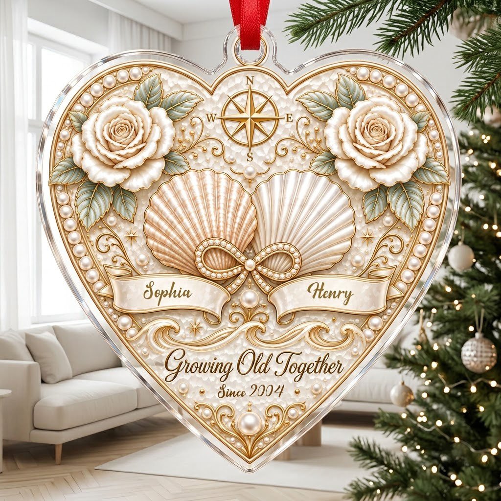 Heart-shaped clear acrylic ornament with seashells, pearl infinity symbol, compass star, and two name ribbons.