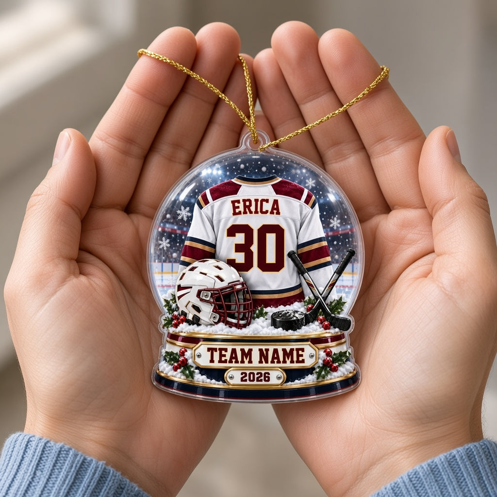 Acrylic snow globe ornament with hockey jersey, helmet, crossed sticks, puck, snowflakes and holly accents.