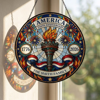 Round stained glass suncatcher with a central torch, fireworks, stars, and a red, white and blue ribbon.