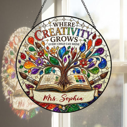 Round stained glass-style suncatcher with tree growing from an open book, paintbrushes, pencils, blossoms, and teacher n