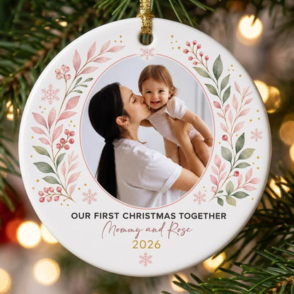 Round ceramic ornament with a photo frame, pink-green botanical wreath, and 'OUR FIRST CHRISTMAS TOGETHER' text.
