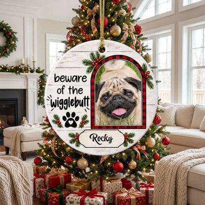 Round ceramic ornament with buffalo plaid photo frame, paw-heart, pine sprigs, and 'beware of the Wigglebutt'.