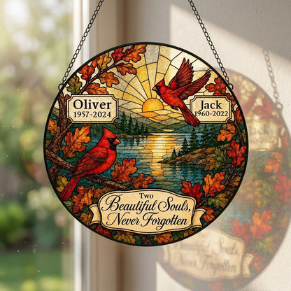 Two red cardinals with a glowing sun over a mountain lake and pine trees, framed by autumn oak leaves on a round suncatc