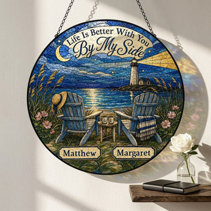 Round stained glass–style suncatcher with two blue Adirondack chairs by water and a lighthouse at night.