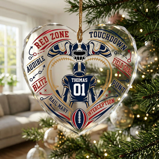 Heart-shaped glass ornament with back-view football player, gold stitched heart frame, football, and play diagram elemen