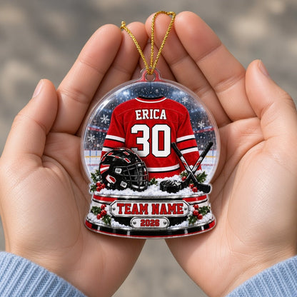 Snow globe acrylic ornament with red and white hockey jersey, black helmet and puck, and a snowy rink backdrop.
