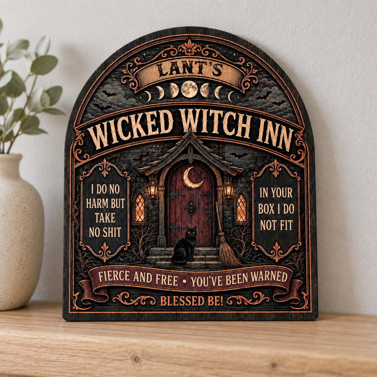 Arch wooden sign with a witch's cottage, bats, moon phases, red crescent door, broom, and a black cat on the steps.